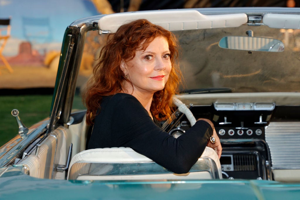 Actress Susan Sarandon turns around in the driver's seat of a convertible to smile at the camera in a black top.