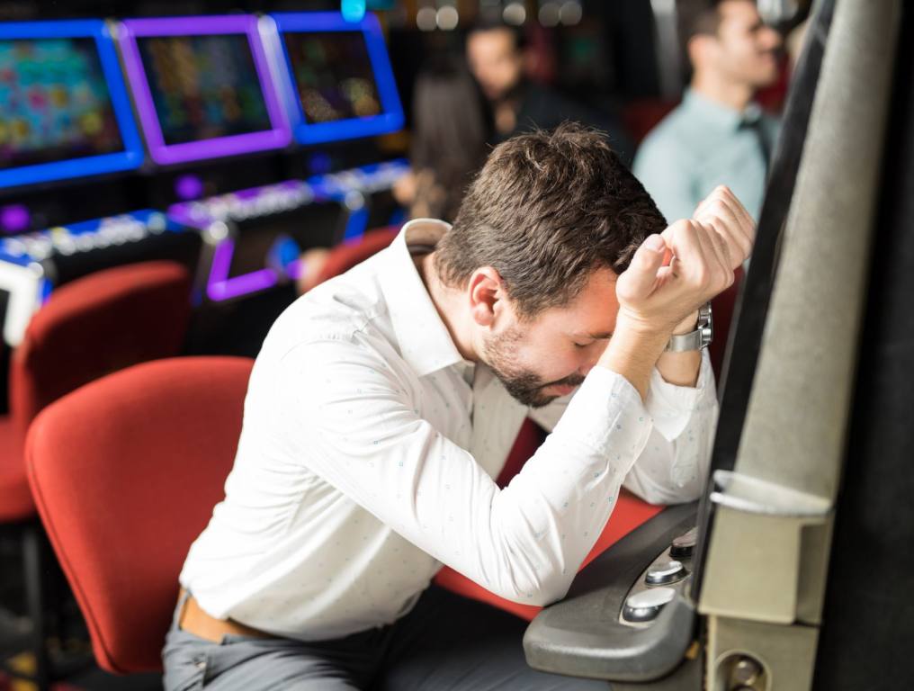 A man in a white button-up shirt leans against his arms on a slot machine upset about a loss. All Las Vegas casinos have slots but not all of them pay out.