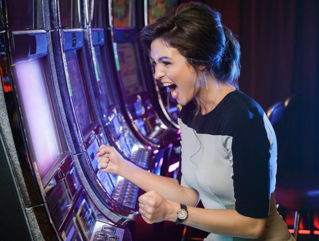 A dark-haired woman sits in front of a slot machine celebrating a win. All of our Las Vegas Casinos have slot machines and table games to keep the fun going. Concept of luckiest casino in Las Vegas.