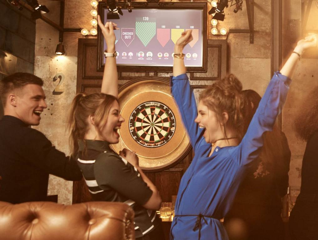 Friends are gathered at Flight Club Las Vegas for a round of darts. They are laughing and throwing their hands up.