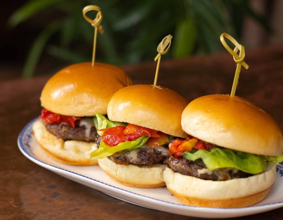 Three prime beef sliders presented on a white plate that sits on a laminate table. One of the menu items at Flight Club Las Vegas.