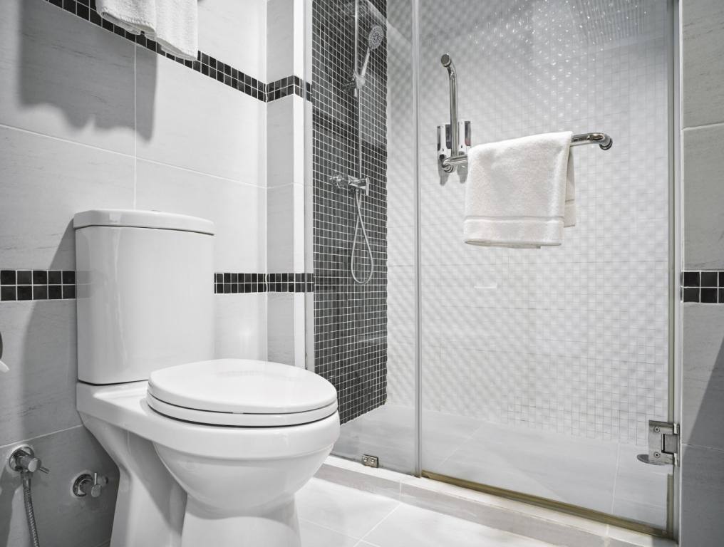 White toilet in at clean bathroom with white tile walls and black tile stripes.