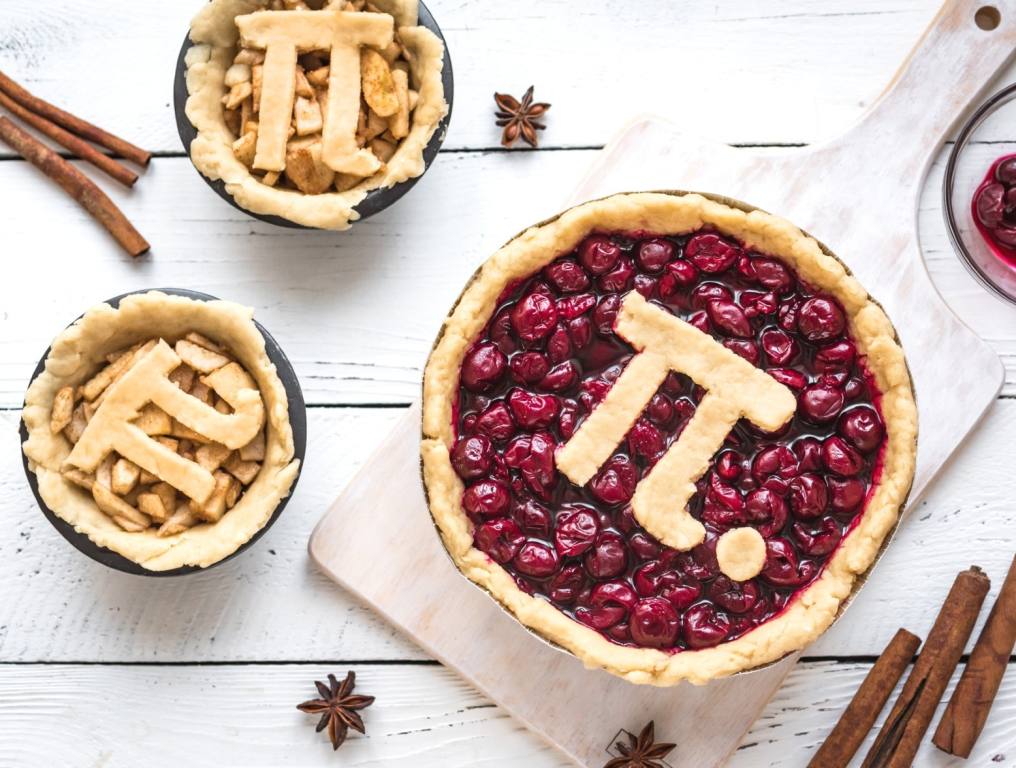 Pi Day Cherry and Apple Pies - making homemade traditional various Pies with Pi sign for March 14th holiday, on white wooden background, top view.