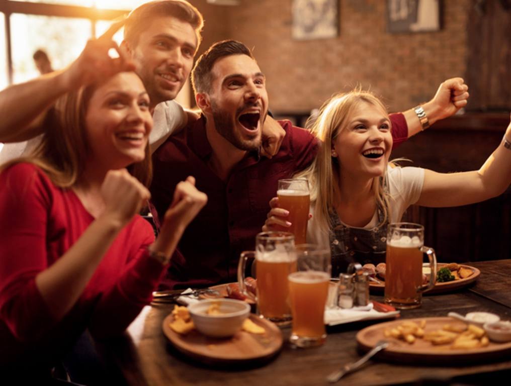 Happy friends cheering for their team while watching sports game on TV in a bar.