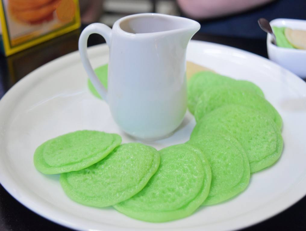 Green sweet pancakes made from flour with sweet sauce on white plate in restaurant. The pancakes are fanned out on the plate, which has a white syrup pitcher in the middle.