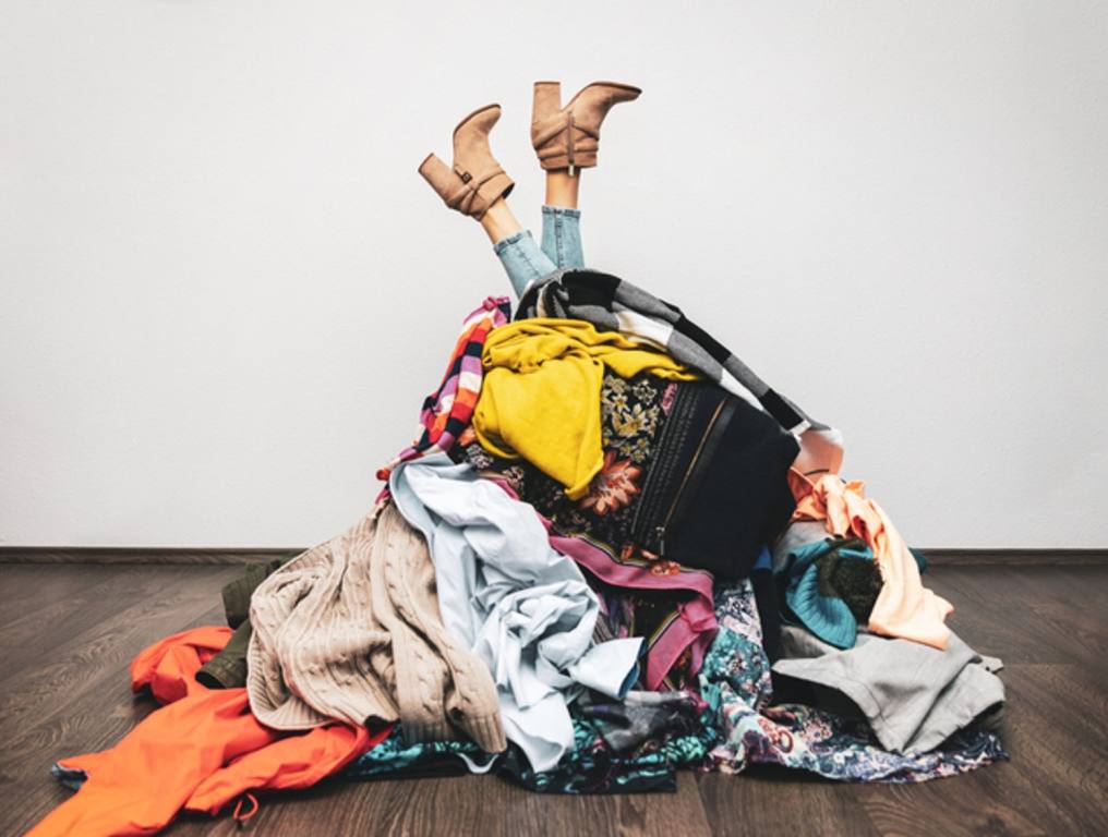 woman legs out of a pile of clothes on the floor. shopping addiction concept