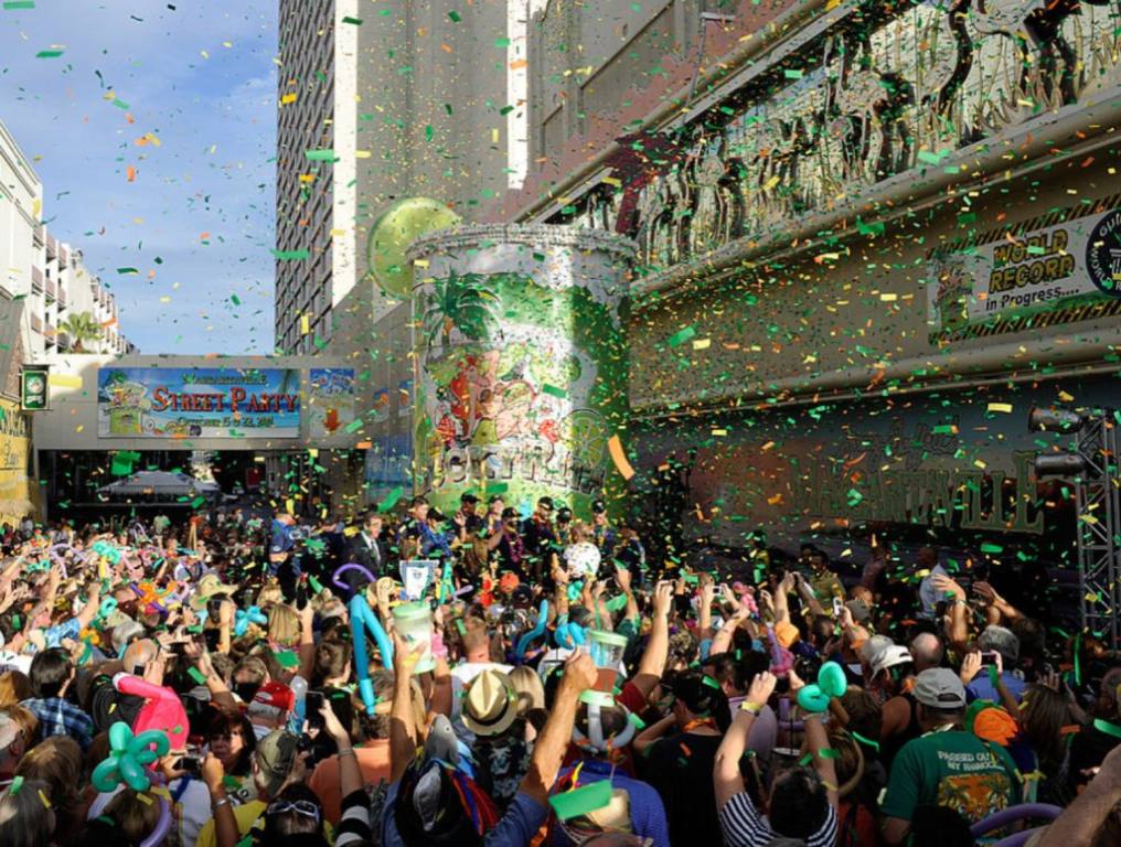 A large crowd of people gather on the street in front of the Flamingo Casino in Las Vegas, Nevada. The are celebrating around a giant margarita . Confetti is flying through the air.