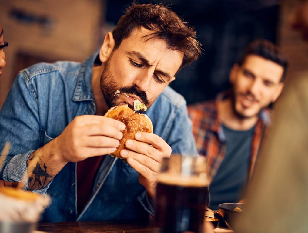 A guy in a blue shirt eating with food coming out of his mouth