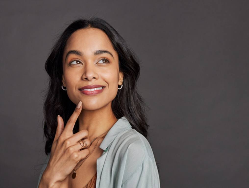 Portrait of pensive young mixed race woman with hand on chin looking away isolated on gray background.