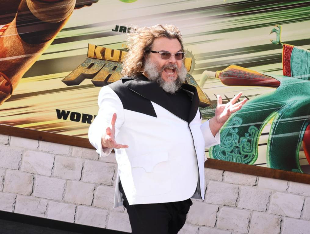 Jack Black attends the premiere of Universal Pictures' "Kung Fu Panda 4" at AMC The Grove 14 on March 03, 2024 in Los Angeles, California. Black is wearing black pants and a white jacket with black collar. He's smiling with mouth open and wearing sunglasses. Black covered a Britney Spears hit for the film.