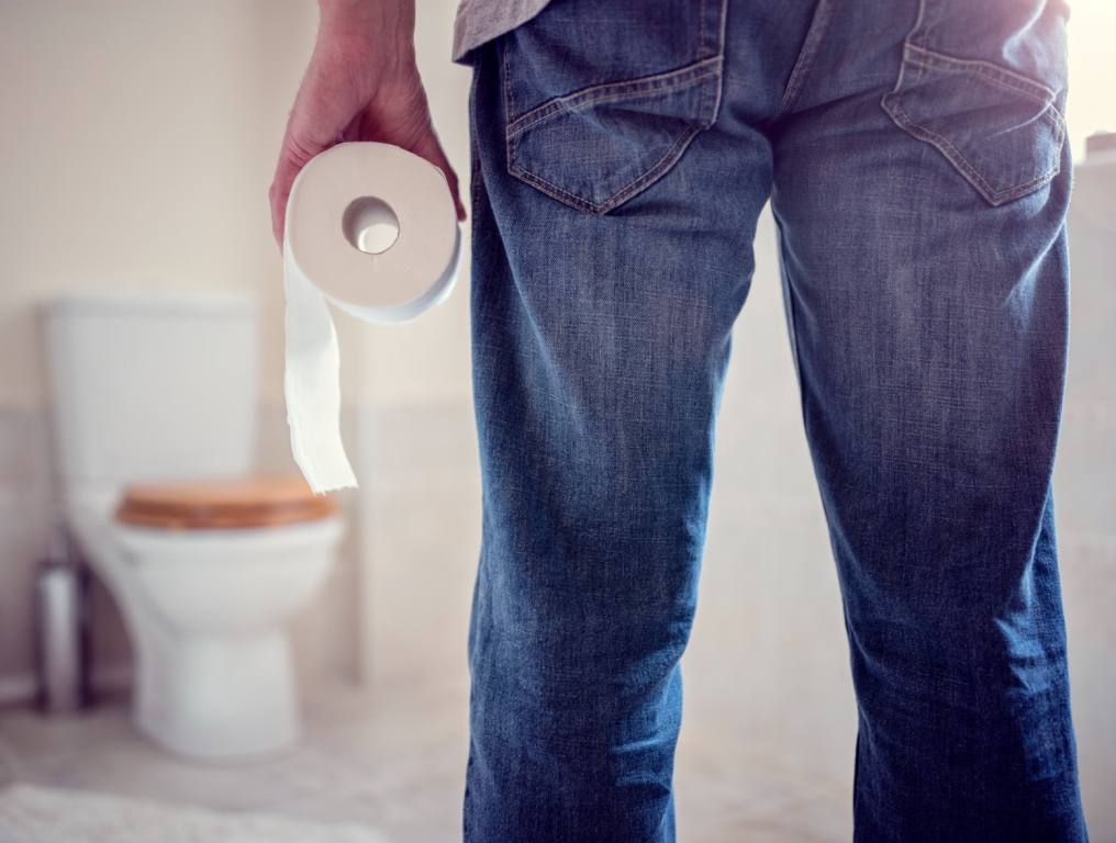 A guy holding toilet paper going into the bathroom