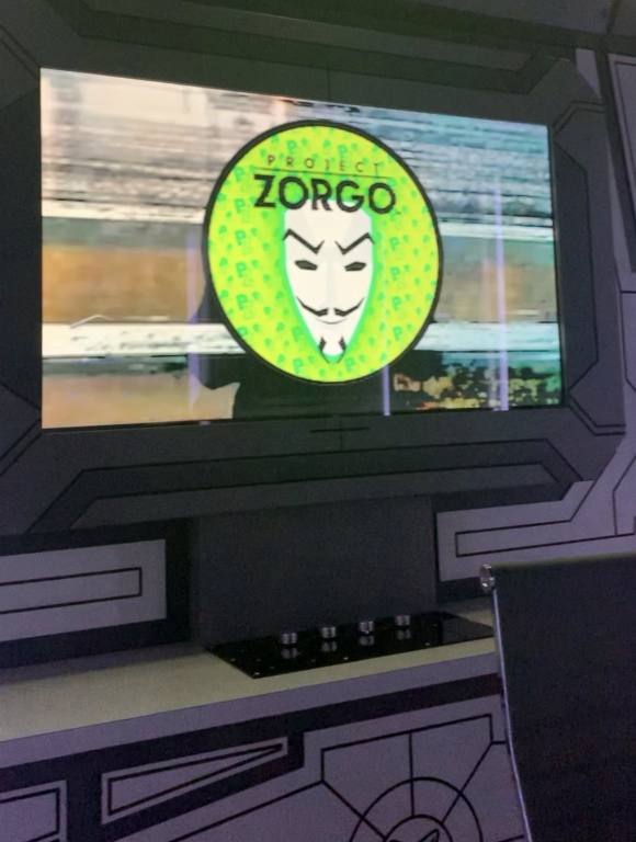 A tv screen is showing a yellow circle emblem with a sinister looking white mask in the middle. The words above the circle read "Zorgo".