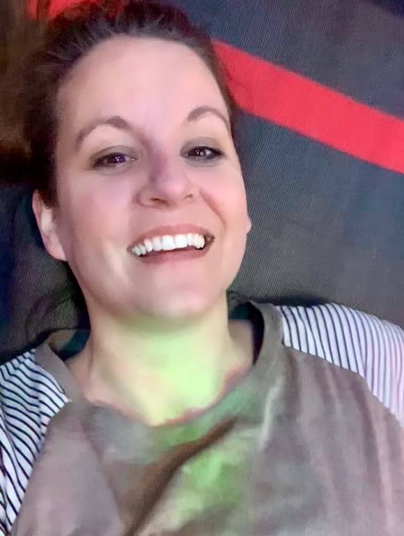 A brunette woman is lying on her back on a trampoline after having been hit by a ball by her opponent. She is smiling, tiredly, and resting before getting back up.