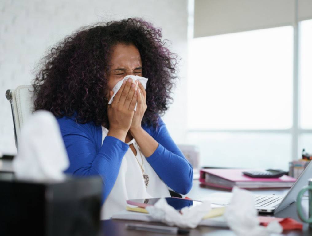 Sick african american girl working from home office. Ill young black woman with cold, sitting at desk with laptop computer and sneezing for allergy, work while sick concept.