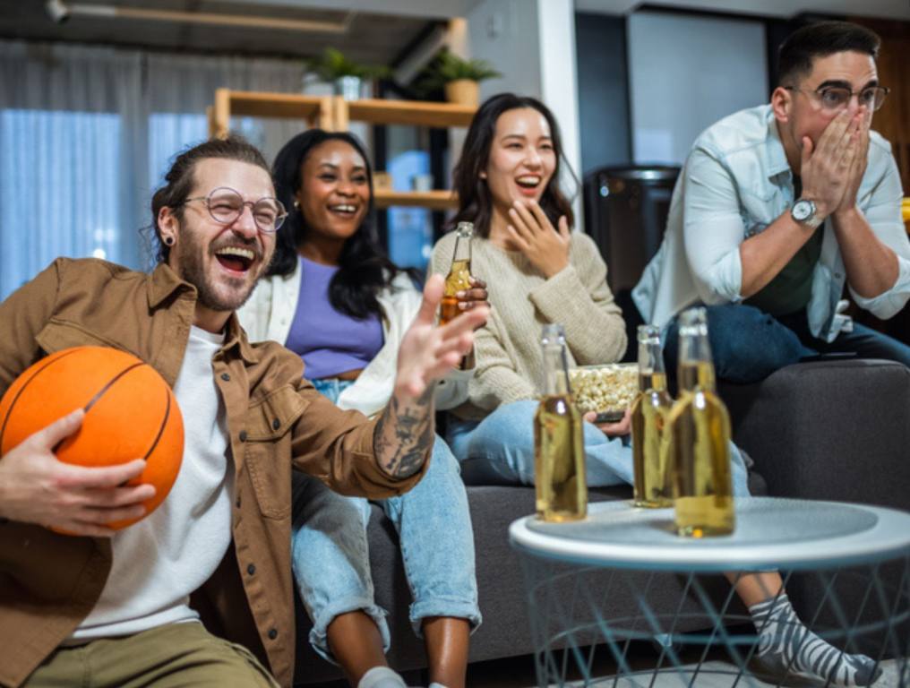 Multiracial group of friends watching basketball game, drinking beer and cheering.