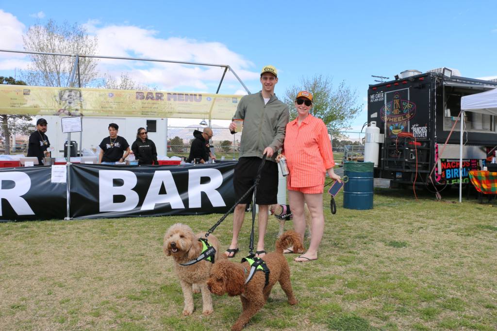 A man and woman pose with their dogs holding alcohol standing in front of the beer booth.