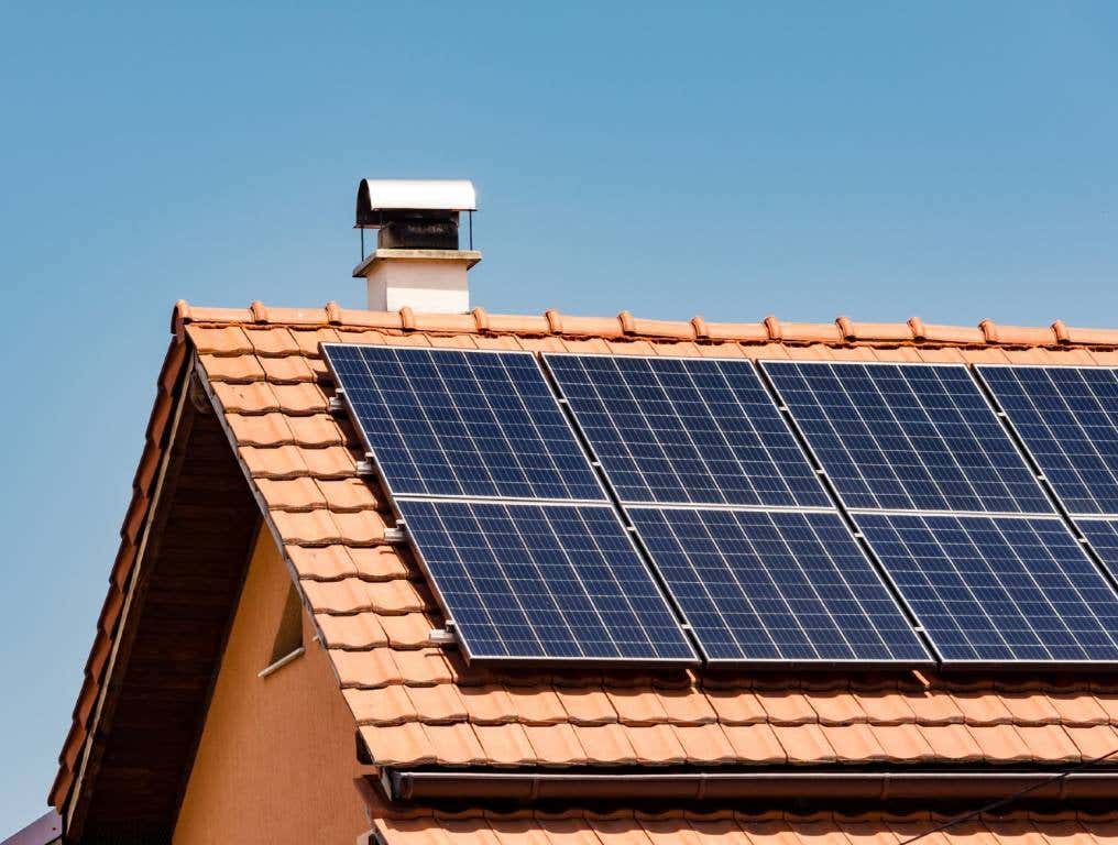 Las Vegas ranks 12th best in the U.S. for solar energy viability. Photo of numerous solar panels that have been installed on the roof of a residential home on top of beige ceramic roof tiles. There is a small chimney on top of the roof at the apex. There is clear blue sky behind the home.