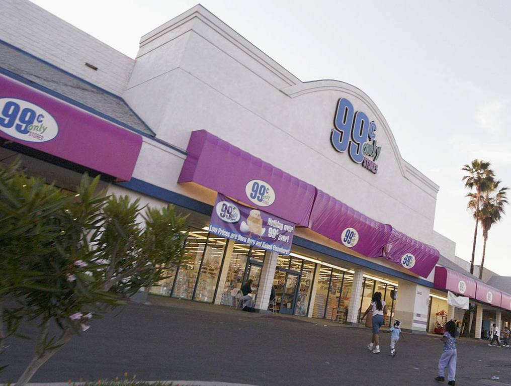 Photo of a 99 Cents Only Store facade. The front of the mall location has lavendar colored awnings above the glass windows and entrance doors. Above the awnings, the company's "99 Cents Only Stores" logo can be seen on the stucco siding. There is a mother and two female children walking from the parking lot towards the front of the store.