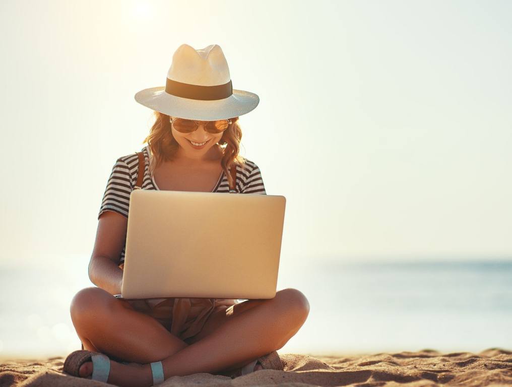 Woman on her laptop at the beach. Here are some in-demand remote jobs that pay more than $100K.