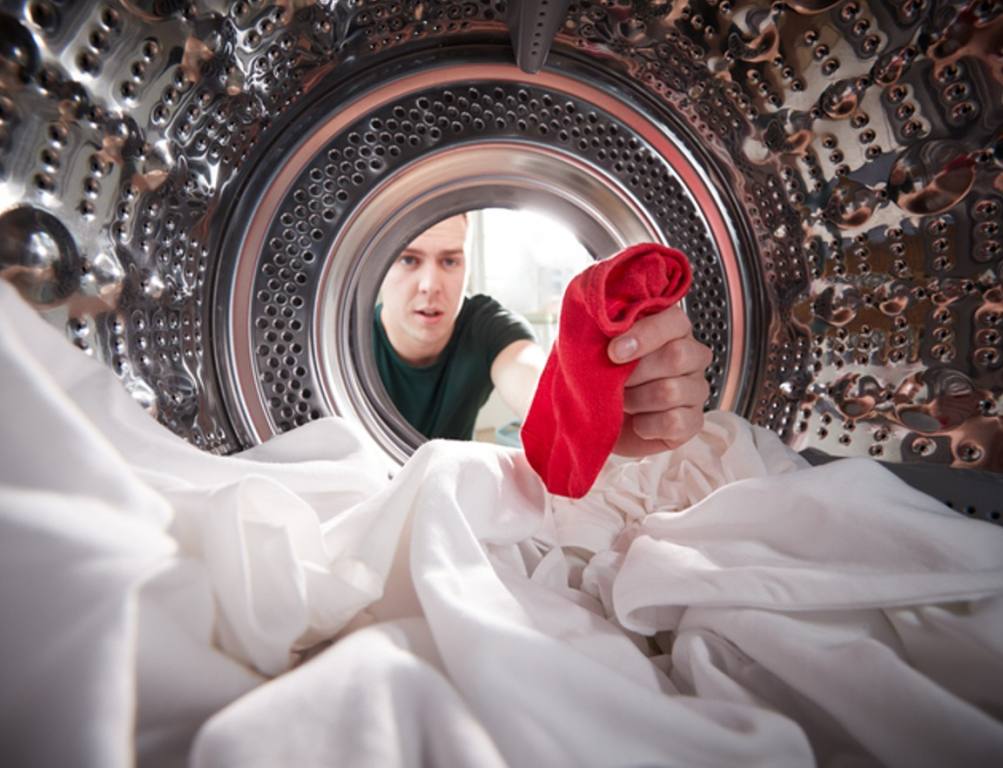 Man Taking Out Red Sock Mixed With White Laundry From Washing Machine, common laundry mistake concept.