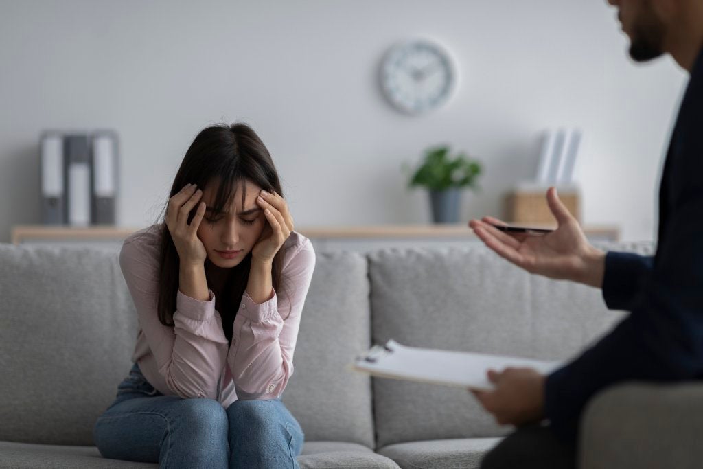 Depressed young woman touching head, seeking professional help with mental disorder at psychotherapist's office. Psychologist having session with desperate female patient. PTSD concept.