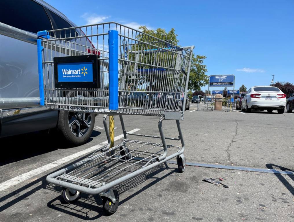 Walmart shopping cart in the parking lot, next to a gray car.