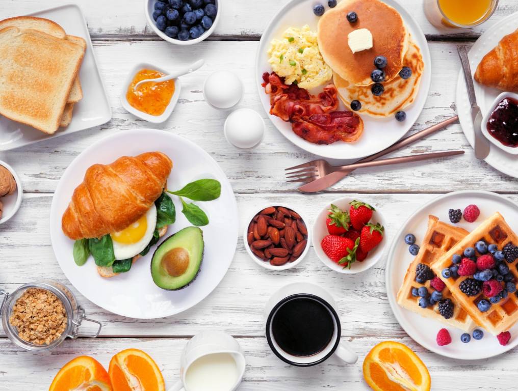 A breakfast spread is laid out on a white wooden table. Various dishes on white plates, including croissants, pancakes, fruit and coffee. Vegas brunch concept.