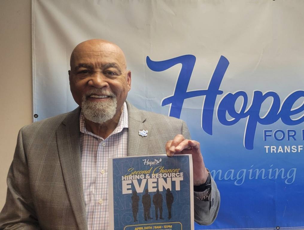 Hope for Prisoners Director of Workforce Development is holding a flyer that reads second chance hiring and resource event offering reentry programs for former inmates