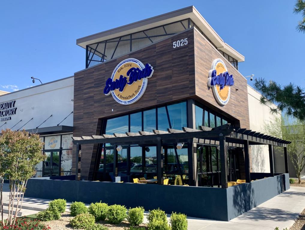 Exterior shot of Early Birds restaurant in Las Vegas. The building is faux rock with the logo. A patio with yellow chairs is in front, below the logo.