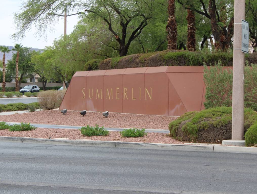 There are fun family events in Summerlin this spring. Photo of a clay-red concrete sign which reads "Summerlin" in gold painted letters. This rectangular sign has been erected on a street corner on the edge of this master-planned community in Las Vegas, Nevada. There are trees, bushes, and clay-red rocks surrounding the concrete sign. One can see the asphalt street in front of the sign. There is also a street sign pole to the right of the Summerlin sign. It is a fairly cloudy day in Las Vegas.