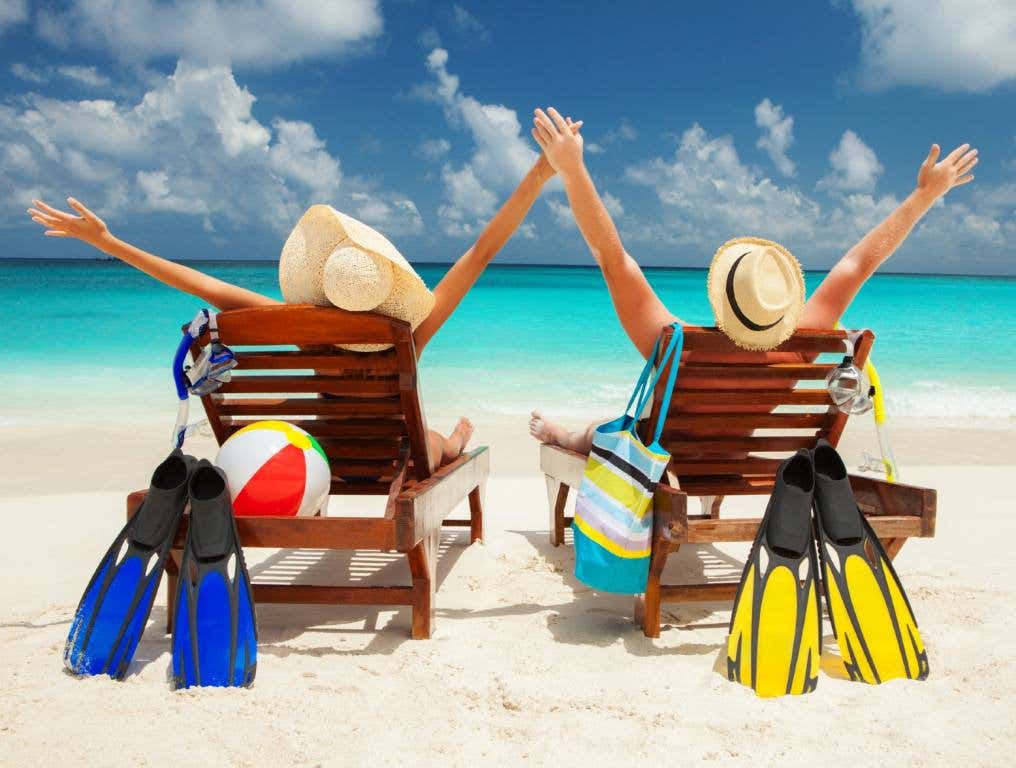 Nevada's favorite vacation destination is the Caribbean. Photo of a happy couple sitting on lounge chairs on a white sand beach. We see the back of their heads and chairs. They are each wearing a straw sun hat. They both have their arms outstretched above their heads. They are looking towards the aqua blue sea. They each have snorkel gear, including fins, masks, and snorkels leaned up against their lounge chairs. The woman on the left also has a beach ball nestled on the back of her chair. The man on the right has a multi-colored beach bag hanging off the left side of his chair.