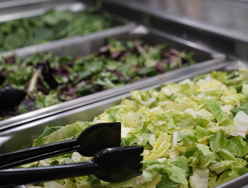 Sweet Tomatoes inspired salad buffet with a tong handing over green lettuce.