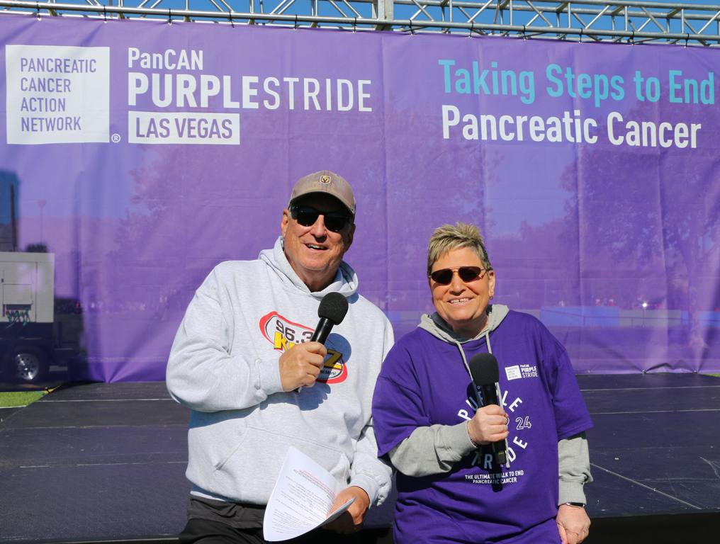 Mike and Carla stand with microphones in front of the stage at PanCAN's PurpleStride 2024 event.