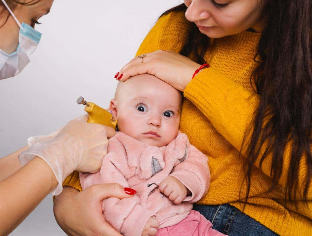 Mother holding her baby while getting her ears pierced.