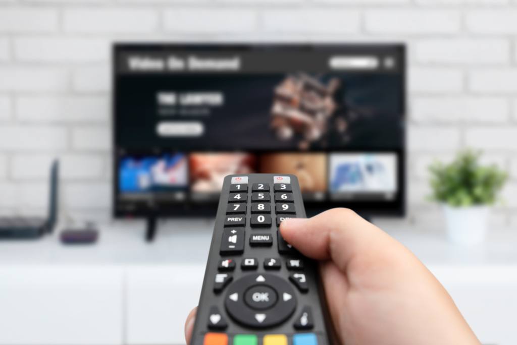 Man watching TV, remote control in hand. VOD service on TV, Notable Titles Coming To Streaming In June.