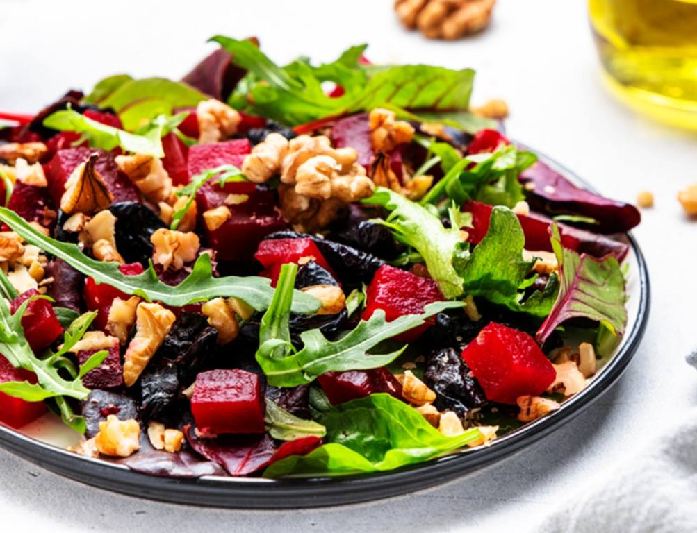 Healthy vegan salad with beetroot, prunes, arugula, chard and walnuts, white table background. Fresh useful vegetarian dish for clean eating, salads