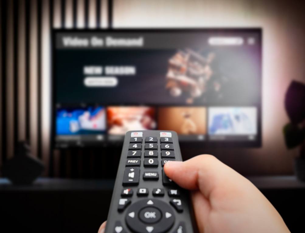 Man watching TV with remote control in hand, person streaming peacock