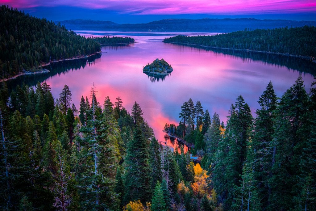 Blues, purples and pinks in the sky at sunset over a lake surrounded by pine trees.