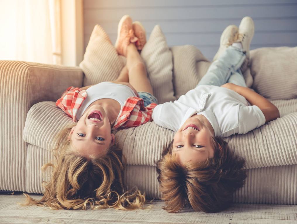 A boy and girl laying upside down on a couch.