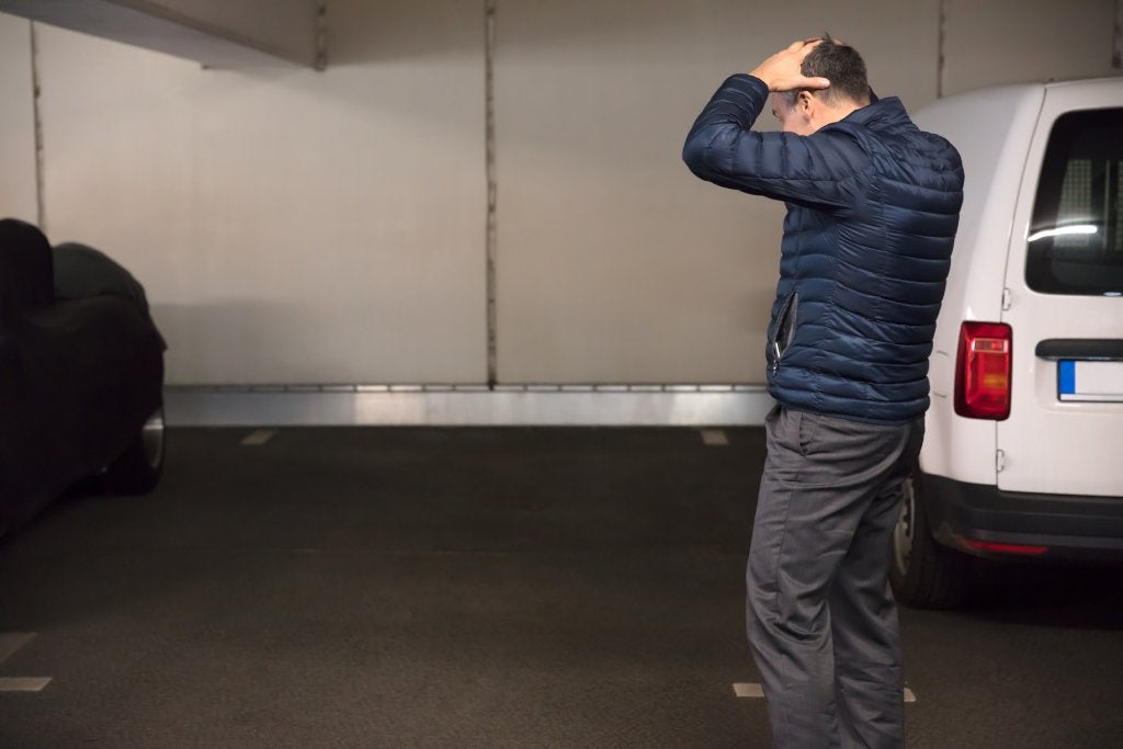 Man stands in a parking garage next to an empty spot between two cars with his hands on his head.