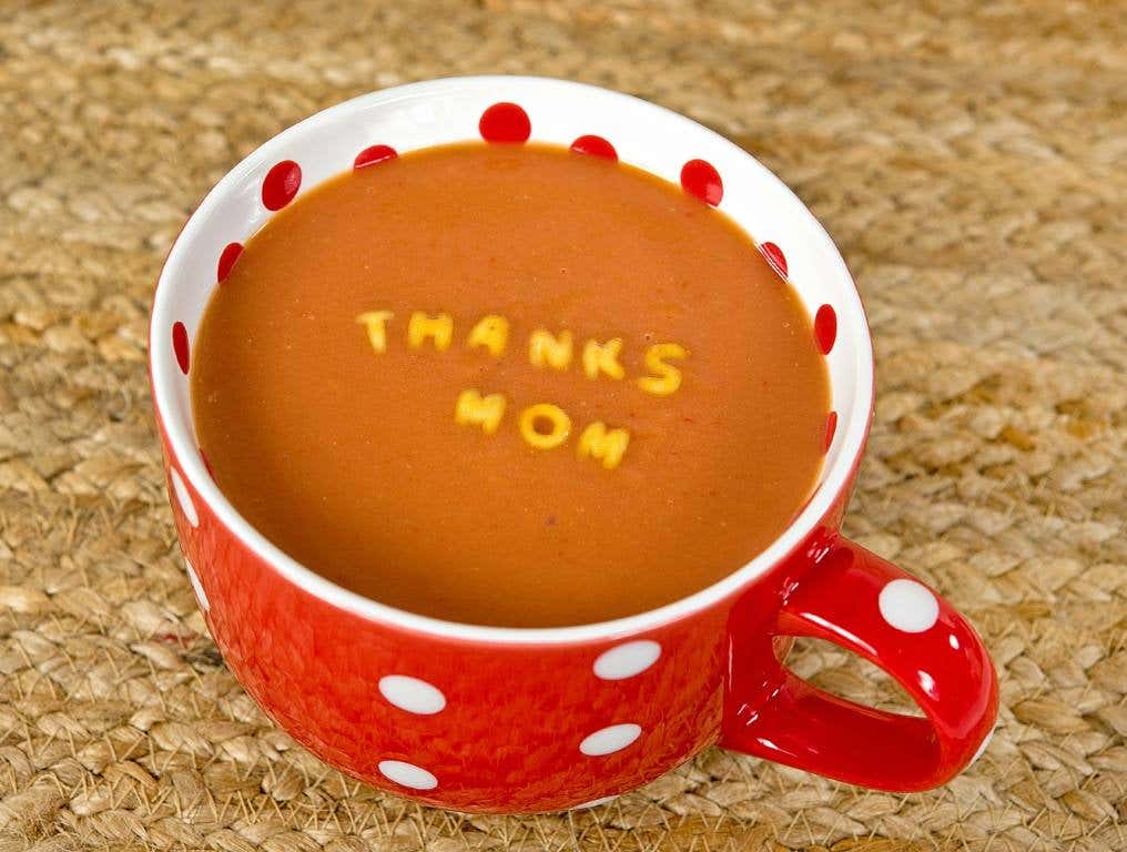 Reasons to say thank mom this Mother's Day. Photo of a red coffee or soup mug decorated with white polka dots outside. The inside of the cup is white with red polka dots. The mug is filled almost to the brim with what looks like alphabet soup. Pasta letters spell out the words "Thanks Mom" on top of the soup.