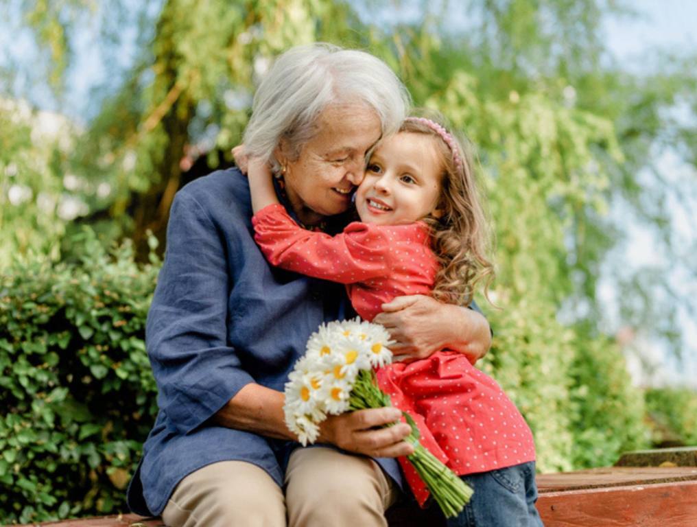 Happy and laughing grandmother and her granddaughter in the park on a bench