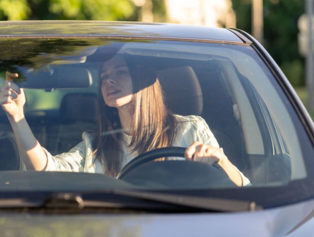 Young woman driver adjust mirror of back rear view inside car before driving holding steering wheel