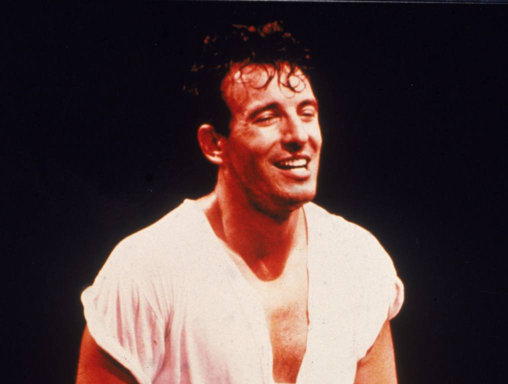 Bruce Springsteen stands onstage, holding an electric guitar at his side during a concert, 1980s.