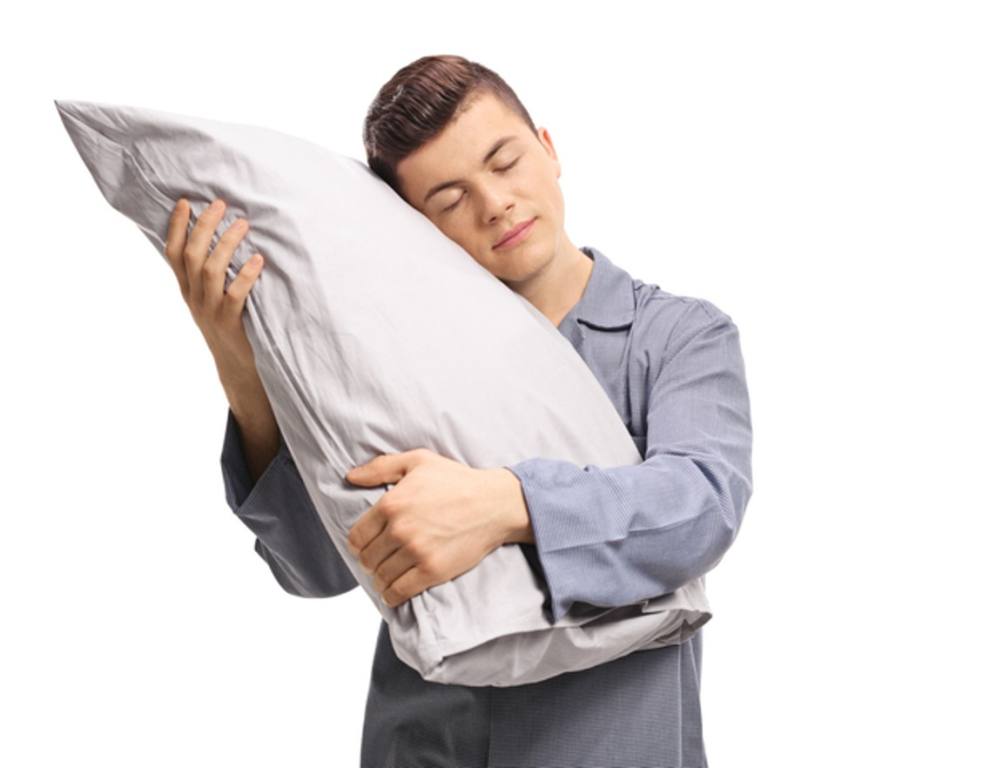 Male teenager hugging a pillow with closed eyes isolated on white background