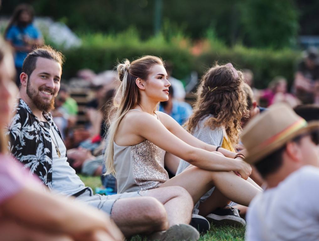 A group of people sit on blankets on the grass looking to the right at an unseen stage. They are watching a show outdoors. Concept: The Little Mermaid at Spring Mountain Ranch.