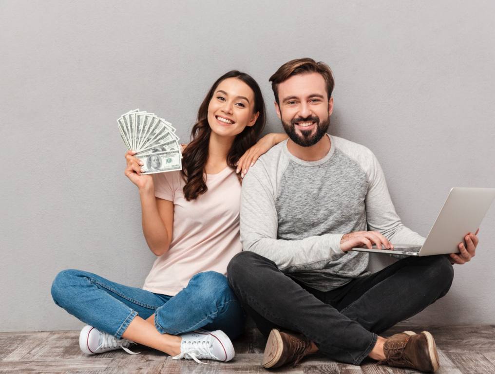 A happy couple sitting on the floor. There are simple habits of millionaires, according to experts, that you can do now to help transform your finances.