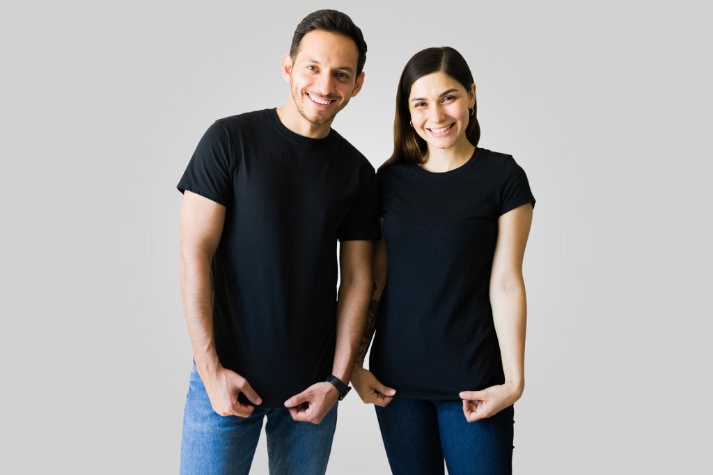 A man on the left and woman on the right are wearing matching black t-shirts and jeans and smiling at the camera.