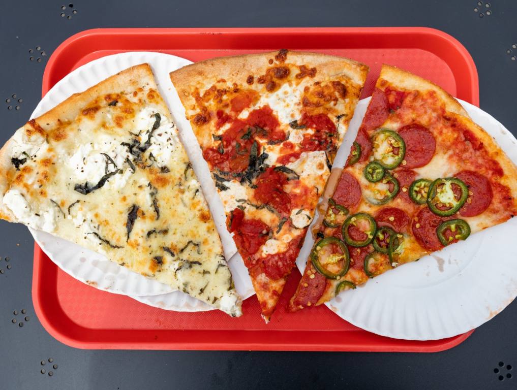 Three pieces of New York style pizza with various toppings sit on a red tray. Concept of Best New York pizza in Vegas.