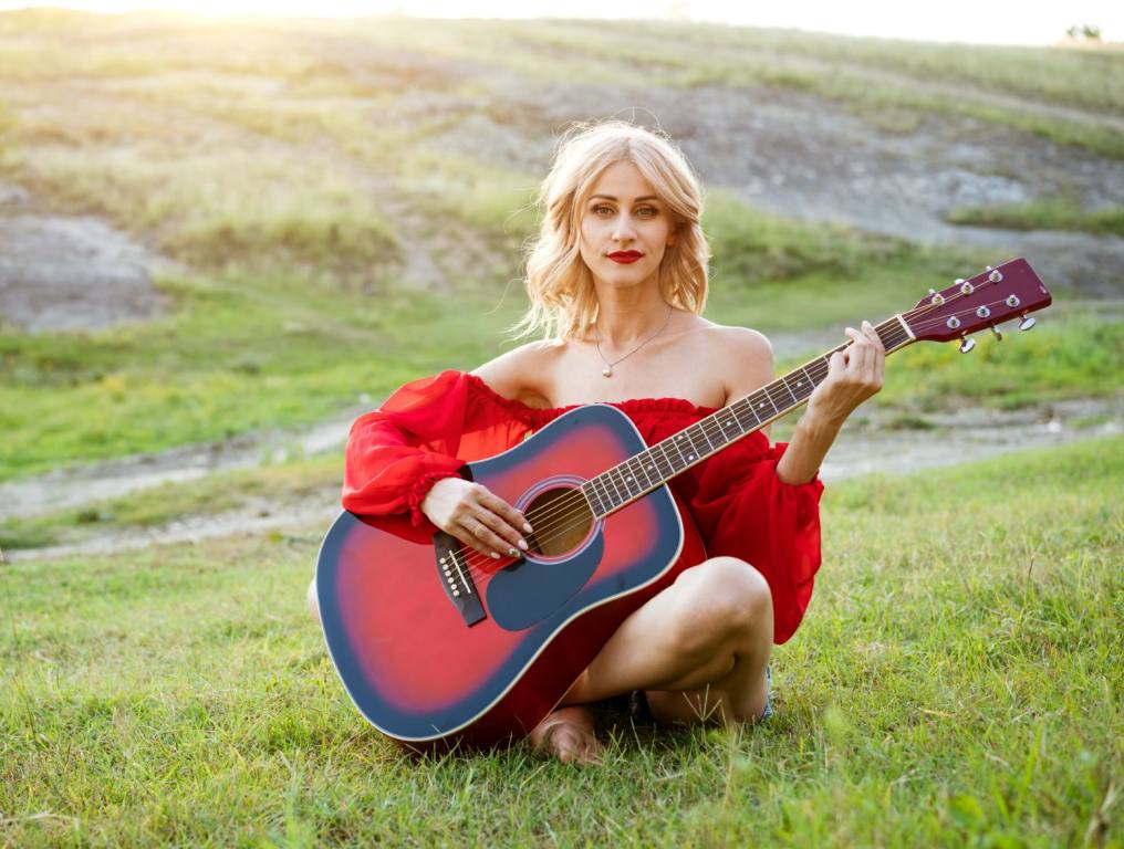 Woman in red dress playing a guitar outside. If you're a musician, you're going to want to use social media to get your music heard.